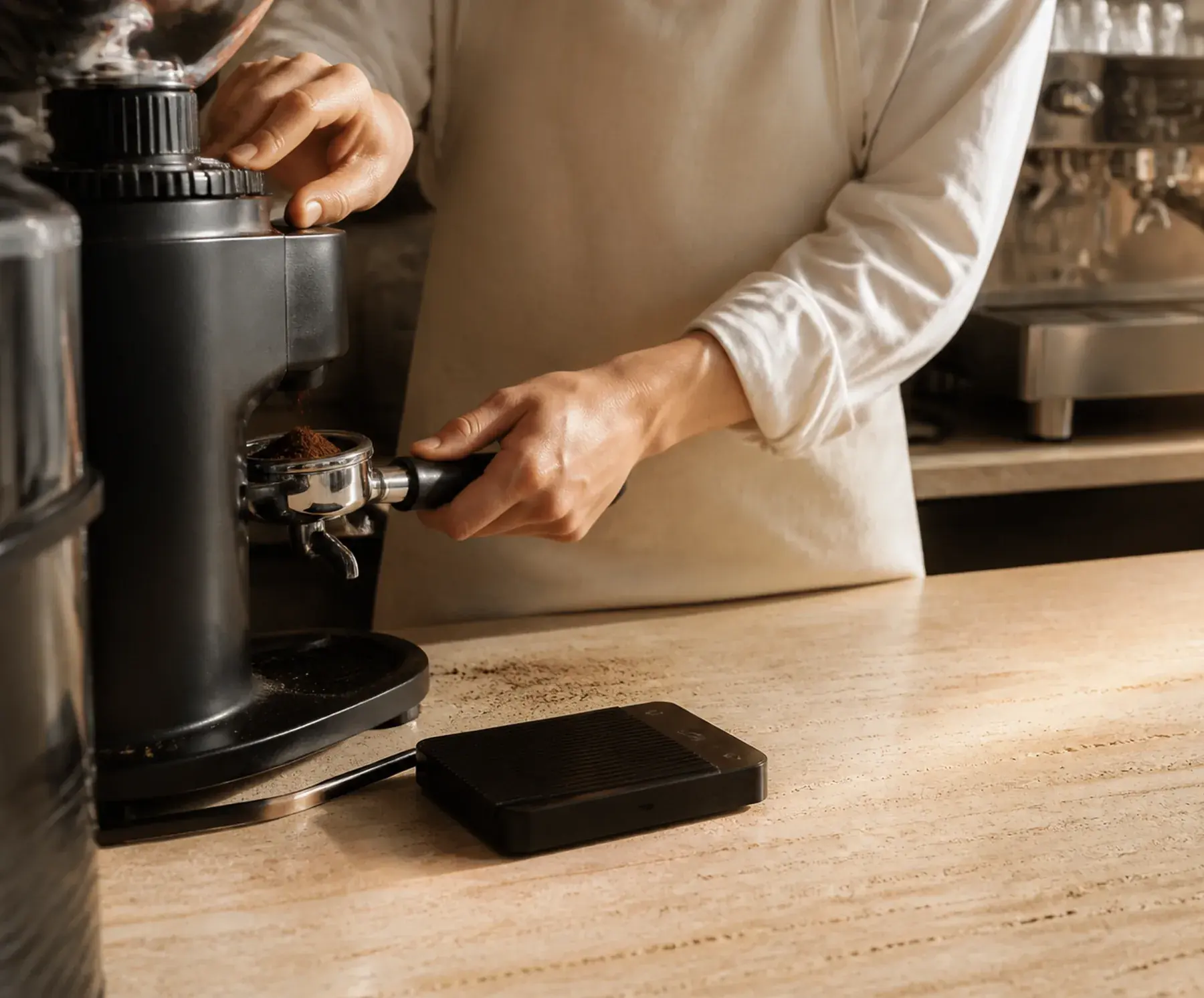 Barista doziranjem puni portafilter mljevenom kafom, uz mlin i vagu na šanku
